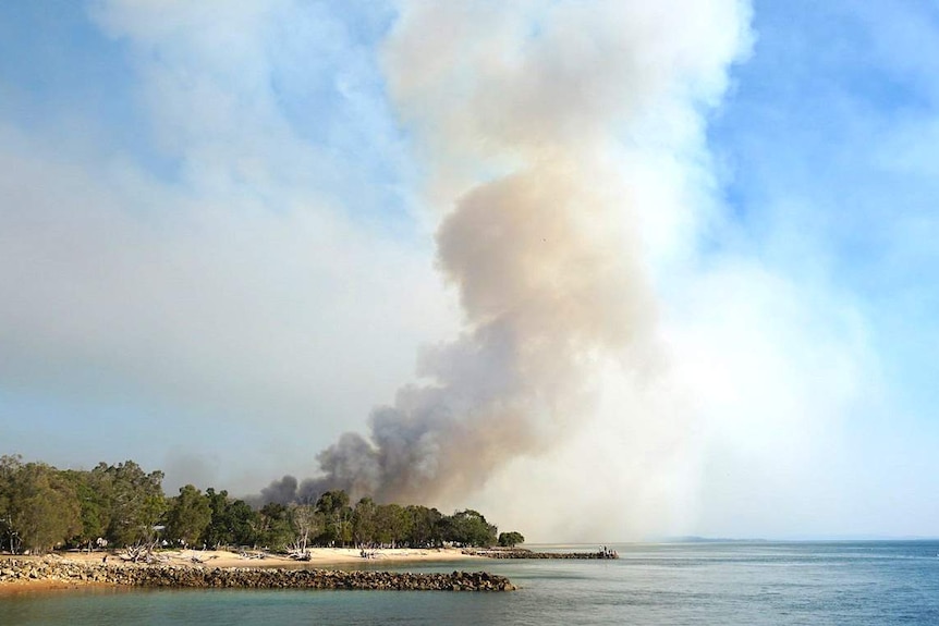 Smoke billows high into the air behind the beach and bush,