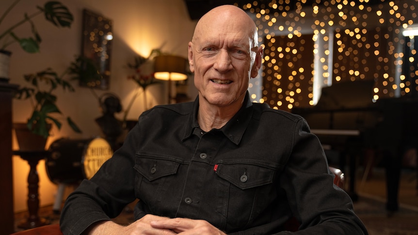 Peter Garrett sitting in a dark room lit by fairy lights with plants in the background.