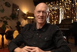 Peter Garrett sitting in a dark room lit by fairy lights with plants in the background.