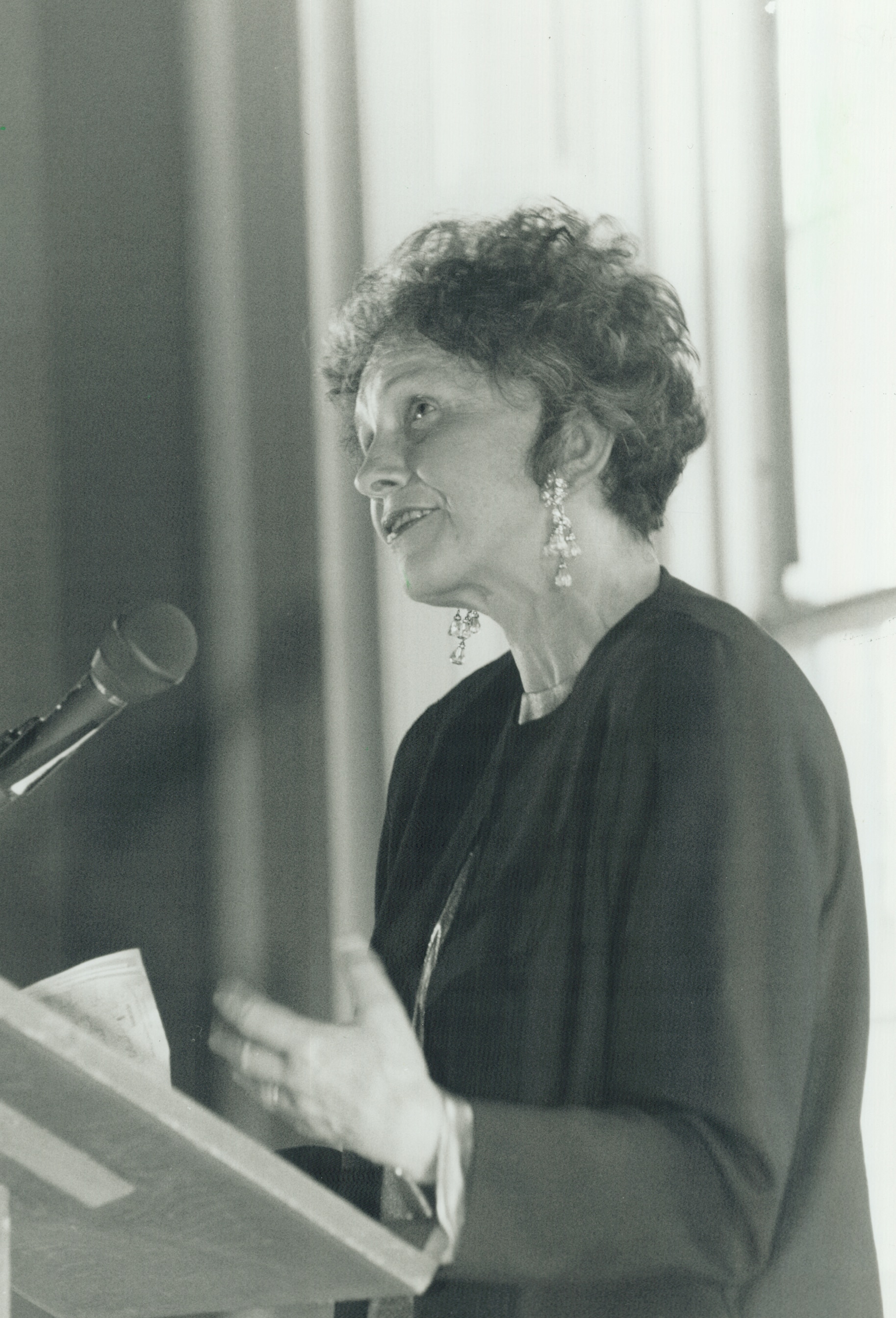 A black and white photograph of a woman speaking at a podium 