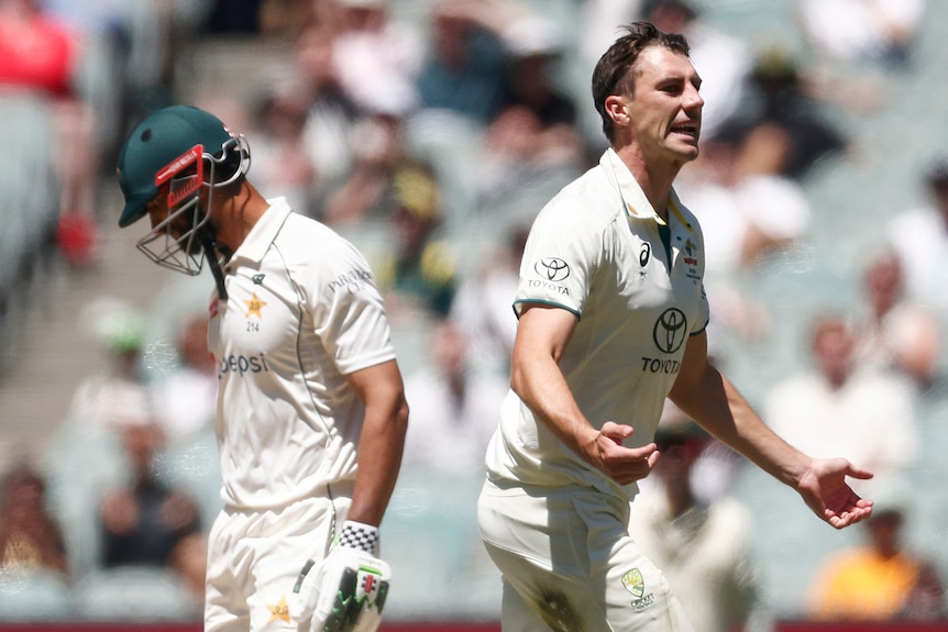 Australia bowler Pat Cummins grimaces as he runs past Pakistan batter Shan Masood at the MCG.