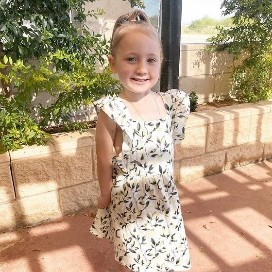 A little girl wearing a white dress smiling at the camera