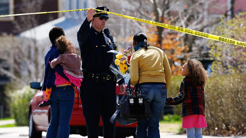 A Boston Police officer lifts the tape for a family to leave flowers at the home of Boston bombing victim Martin Richard.