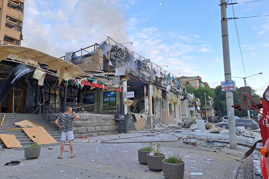 Man stands on a street in front of a shop and restaurant destroyed by a Russian missile attack