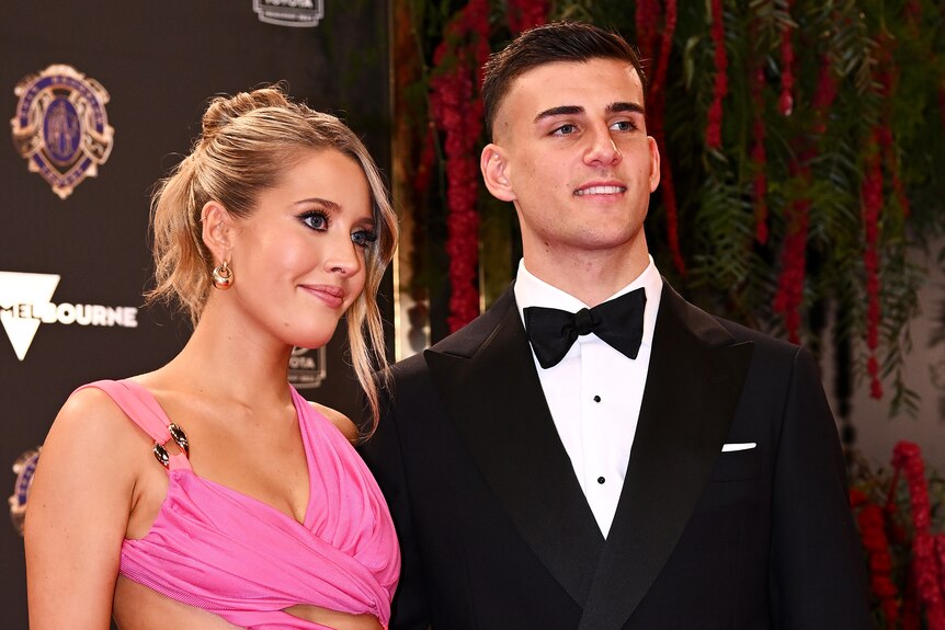 Collingwood AFL player Nick Daicos stands wearing a tuxedo next to a woman in a pink dress before the Brownlow Medal ceremony.