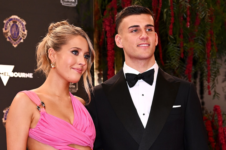 Collingwood AFL player Nick Daicos stands wearing a tuxedo next to a woman in a pink dress before the Brownlow Medal ceremony.