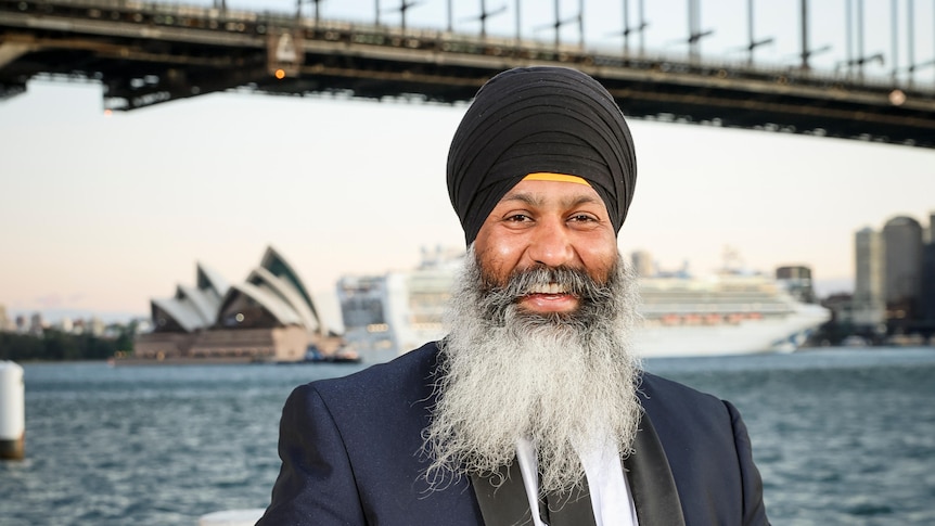 portrait of amar singh smiling in formal suit with beard and Sikh turban standing in front of sydney opera house