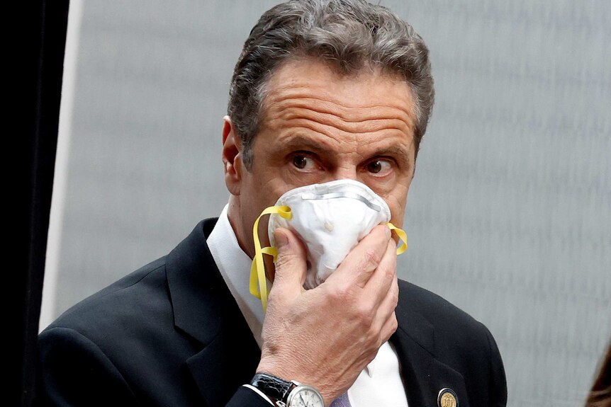 Andrew Cuomo holds a protective mask to his face.