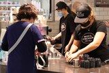 a woman receiving a coffee at a cafe with masked workers