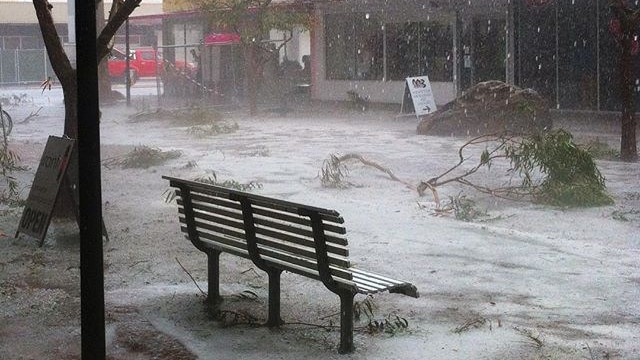 A street in the middle of Alice Springs is coated white with hail and branches are strewn around.
