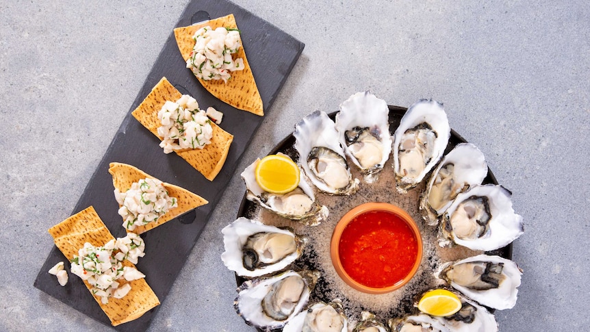 A slate platter of namas on crispbread alongside a circular platter of oysters.