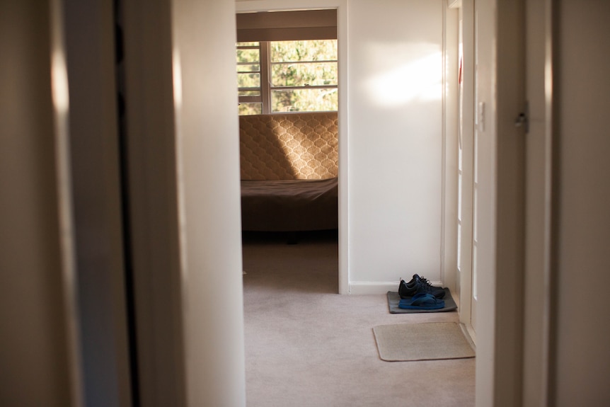A hallway looking down into a bedroom, shoes sit near the door