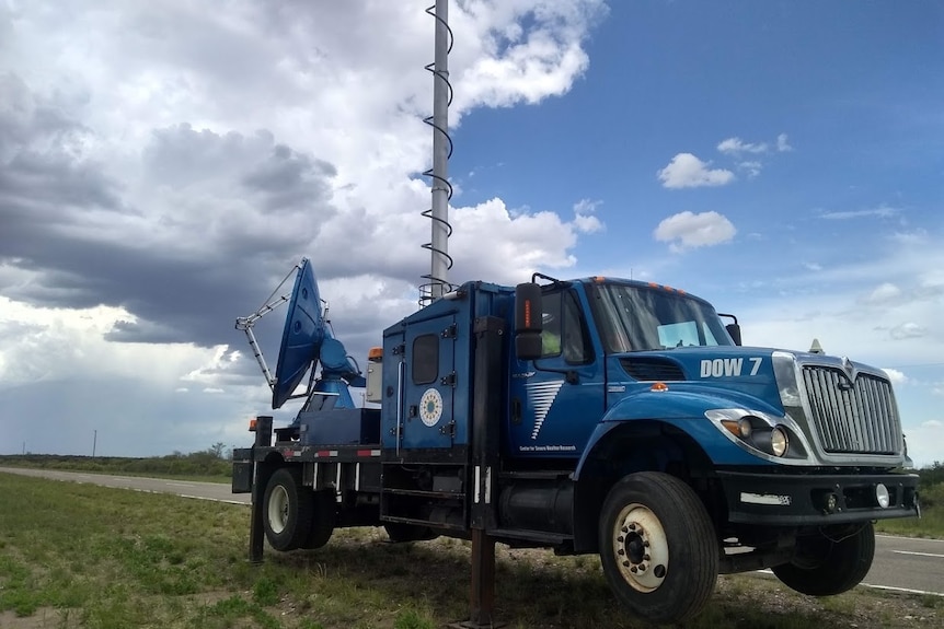 A truck with weather radar mounted parked on the side of the road.