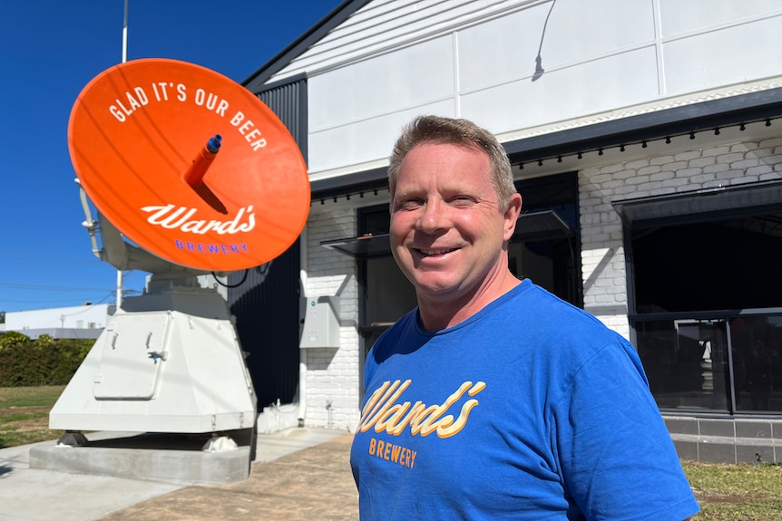 A man stands outisde an old drinks factory with an orange weather radar behind him 