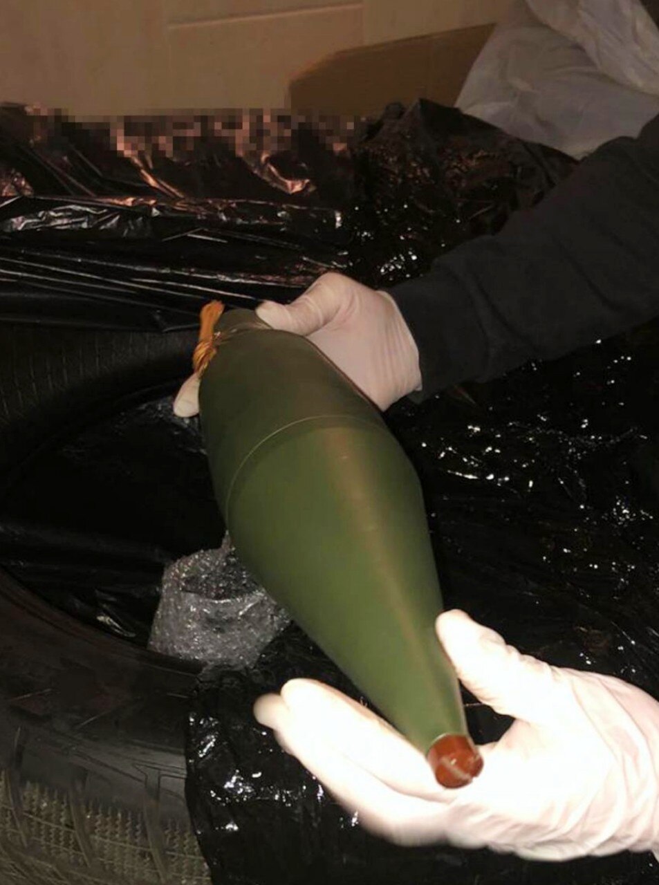 A person's hands wearing gloves, and holding a large bomb.