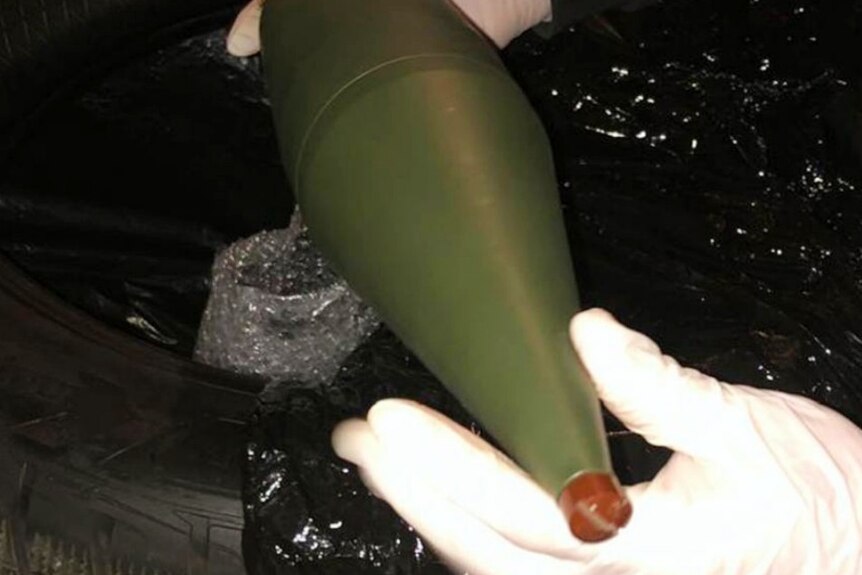 A person's hands wearing gloves, and holding a large bomb.