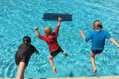 Three children jumping into a swimming pool.