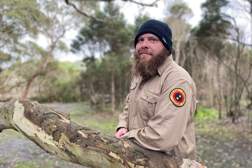 Pakana ranger Brendan Lowery wearing his uniform, leaning on a tree in the Preminghana bushland.