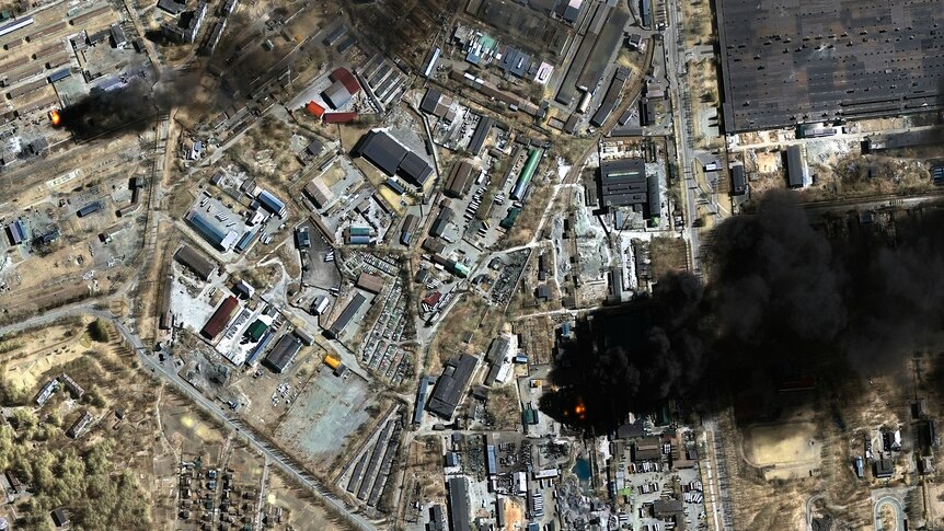 An image taken by satellite shows the layout of the town with a large dark pool of smoke on the right side of the image.