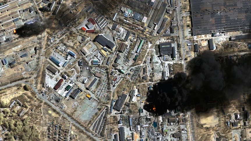 An image taken by satellite shows the layout of the town with a large dark pool of smoke on the right side of the image.