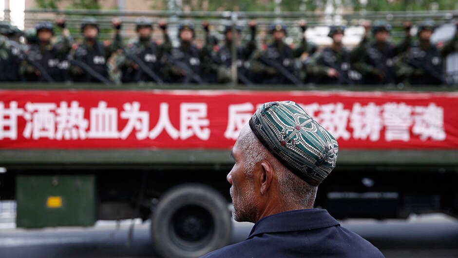 A Uighur man looks on as a truck carrying paramilitary policemen travel along a street during an anti-terrorism rally in China.