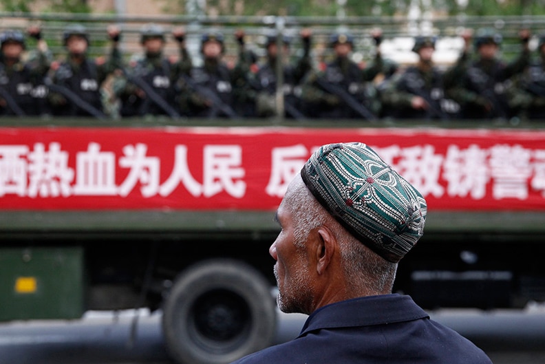 A Uighur man looks on as a truck carrying paramilitary policemen travel along a street during an anti-terrorism rally in China.