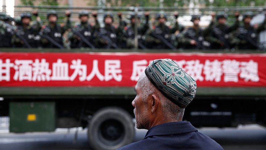 一名维吾尔男子看着一辆载有准军事警察的卡车在中国反恐集会期间沿着街道行驶。