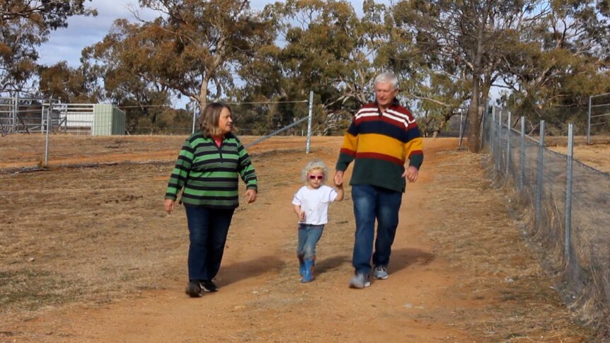 Helen and Korrie Kueper walk towards the camera on their farm, with their grand-daughter walking in between.