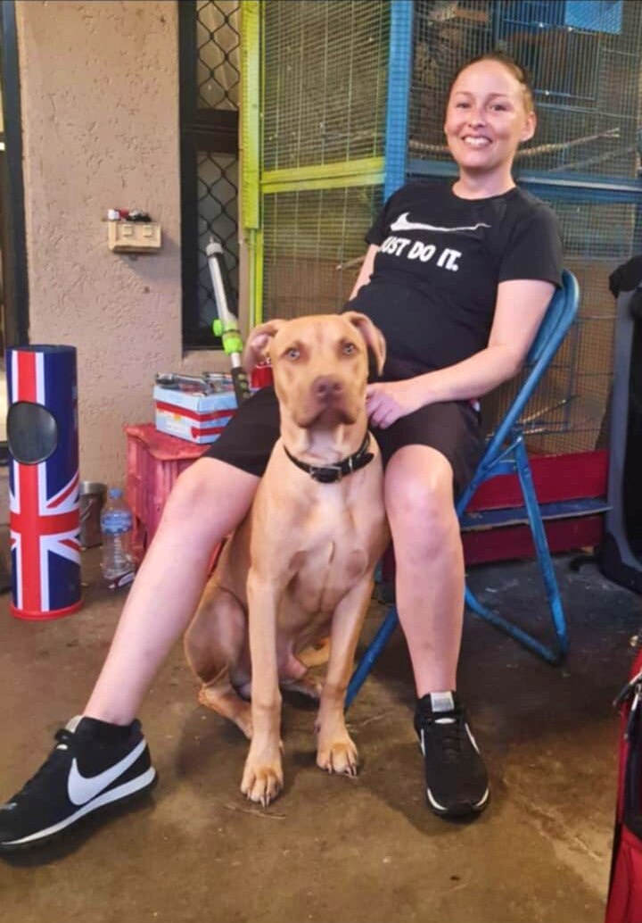 A woman wearing a black Nike just do it t-shirt sits on a blue chair and holds a brown dog