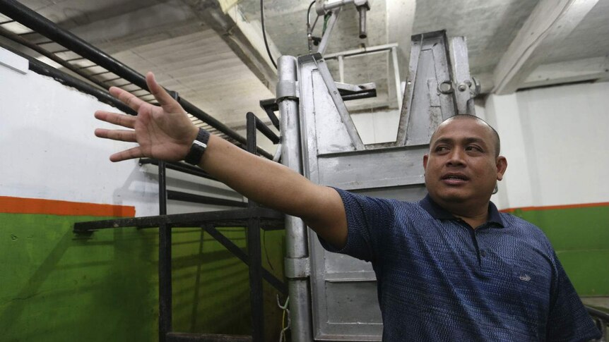 A man gives a tour of an empty metal restraint box in an empty abattoir.