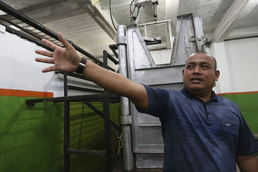 A man gives a tour of an empty metal restraint box in an empty abattoir.