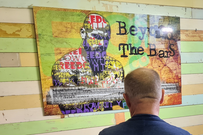 An inmate looks at an artwork that includes text saying "Beyond the bars".
