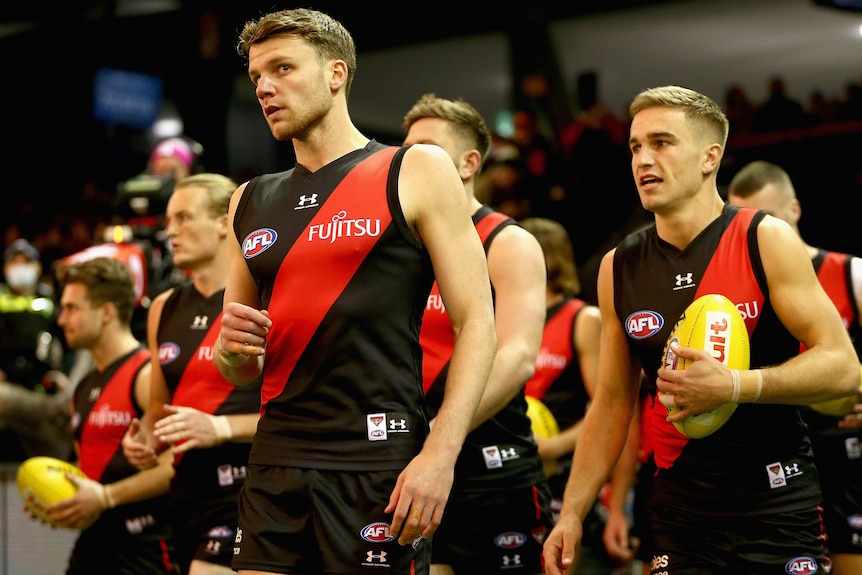 A group of Essendon AFL players hold footballs as they prepare to run onto the field.