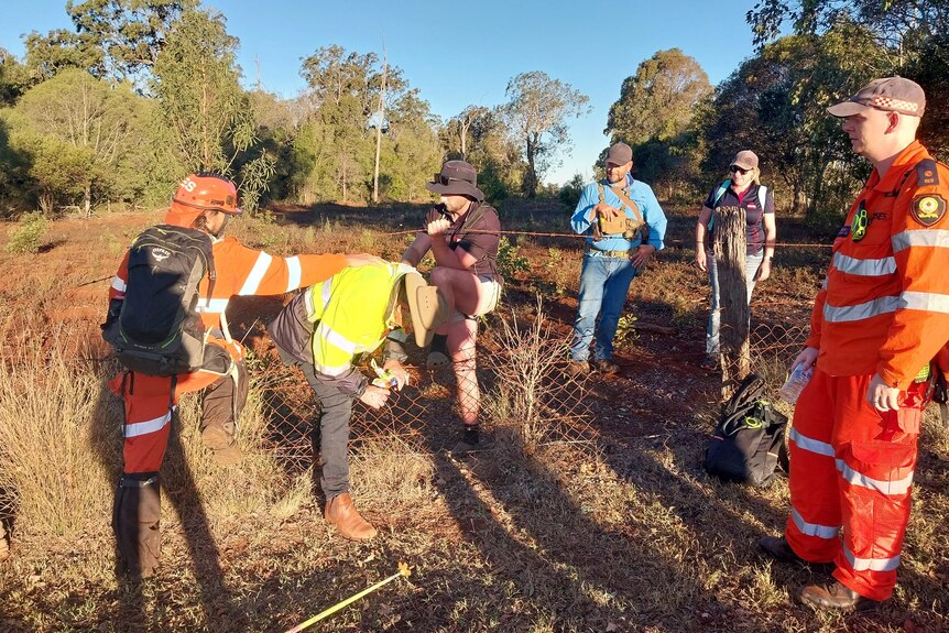 A man climbs through a wire fence assisted by an SES volunteer.