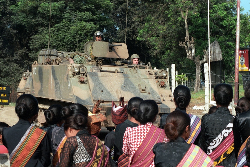 An army tank watched by people in cultural dress.