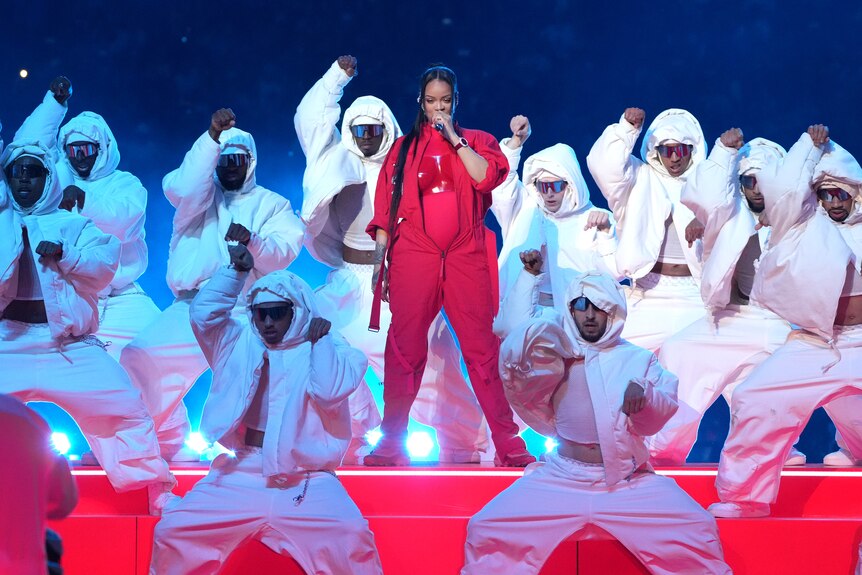 Rihanna sings, dressed in red and surrounded by dance troup dressed in white