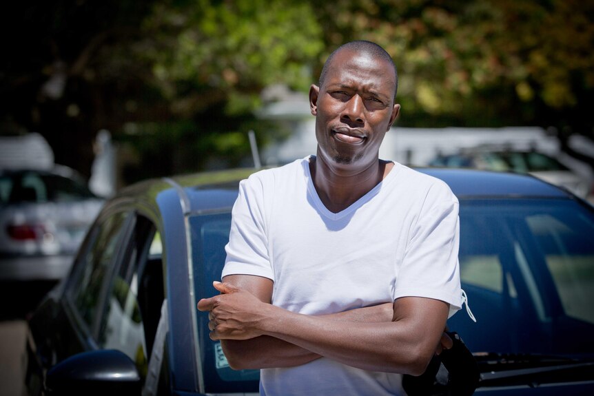 Misheck Mabheka leans on the bonnet of his car in a parking lot in Cape Town.