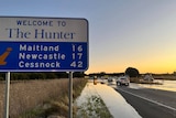 A sign saying welcome to the Hunter next to a flooded road