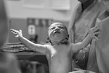 Monochrome of newborn baby reaching out seconds after birth.