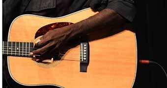 A close up of Australia's most prominent indigenous musician, Dr G Yunupingu, strumming a guitar.