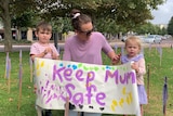Mum between two children with a sign that says "Keep Mum Safe"