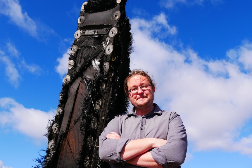 A man stands in a paddock next to a large piece of debris