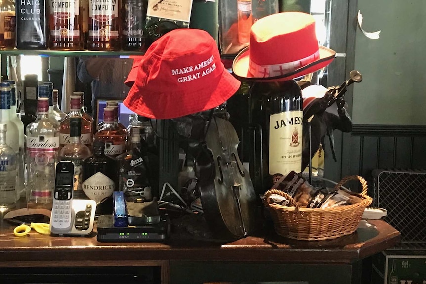 Red hats sit on top of whisky bottles and a violin on a bar lined with liquor