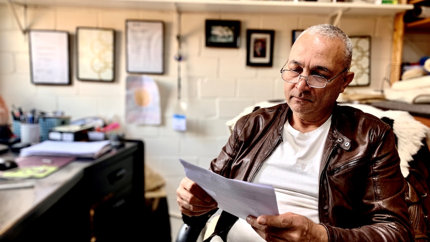 A man wearing a leather jacket and glasses looks at paperwork.
