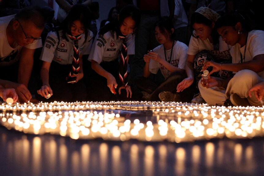 Girl scouts light tea candles to illuminate a room in which lights have been switched off.