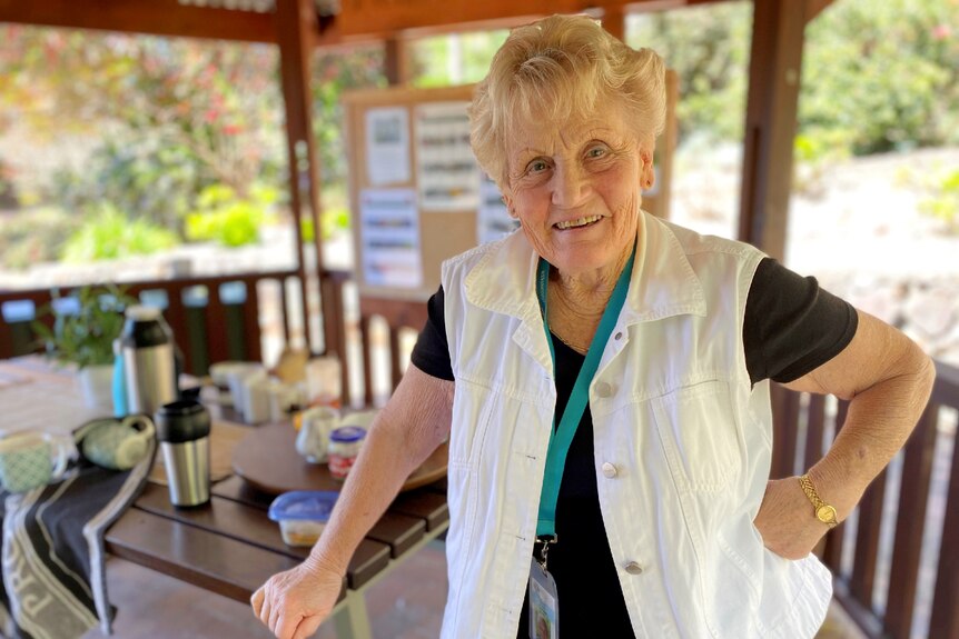 Woman stands beside a picnic table, hand on hip, smiling