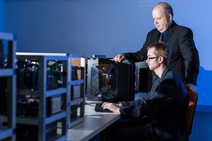 A man in a suit looks at a computer with a student.