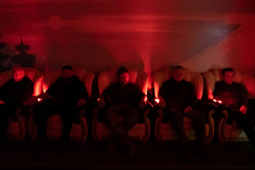 People are resting on chairs in the dark with red light shining on them. 