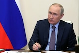 Sitting in front of a russian flag, Putin listens holding a pen