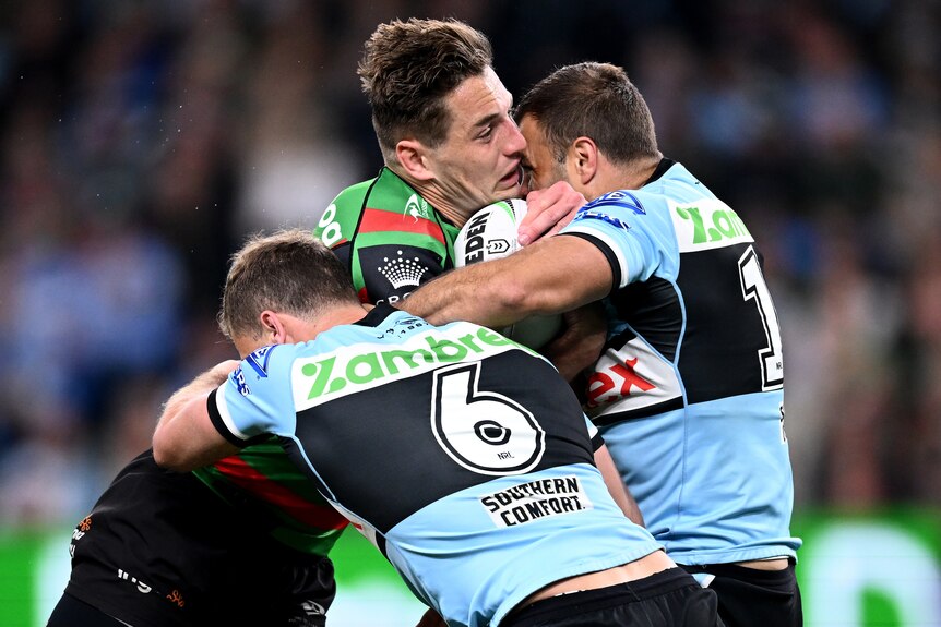 A South Sydney NRL player is tackled by two Cronulla opponents.